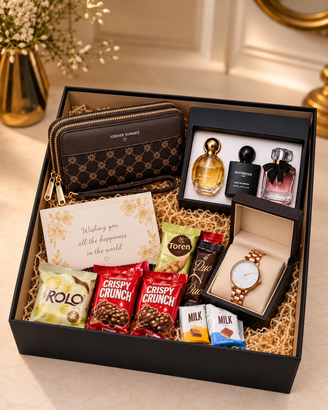 Open black gift box with a brown wristlet purse, three-piece perfume set, rose-gold wristwatch, assorted chocolates and a floral greeting card, neatly arranged in cream shredded paper.